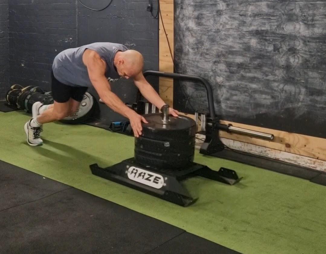 Jason pushing a weighted sled along a strip of green turf in the gym